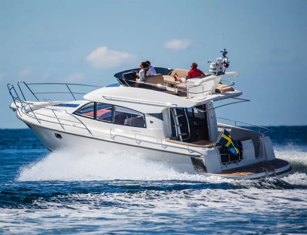 A luxury motorboat speeds across the water with passengers enjoying the sun on deck against a clear blue sky.